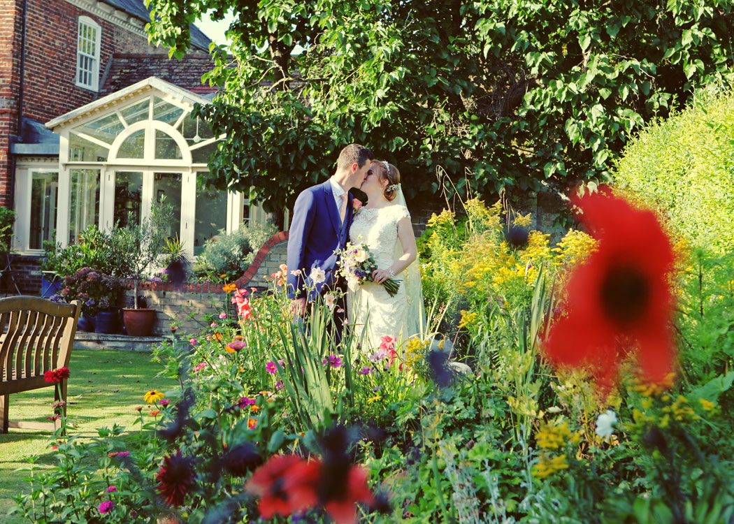 A bride and groom kissing in a flowerbed on their wedding day photographed by Suffolk Wedding Photographers Hayley Denston Photography