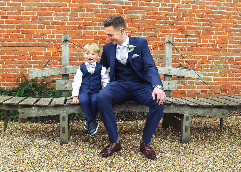 A groom and his pageboy sat on a bench waiting for his wedding ceremony at Haughley Park Barn Wedding Venue photographed by Suffolk Wedding Photographers Hayley Denston Photography