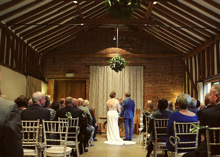 A bride and grooms wedding ceremony taken from the back of the room at Haughley Park Barn Wedding Venue photographed by Suffolk Wedding Photographers Hayley Denston Photography