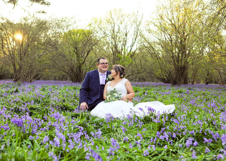 A bride and groom sat in the bluebell woods together at sunset at Haughley Park Barn Wedding Venue photographed by Suffolk Wedding Photographers Hayley Denston Photography