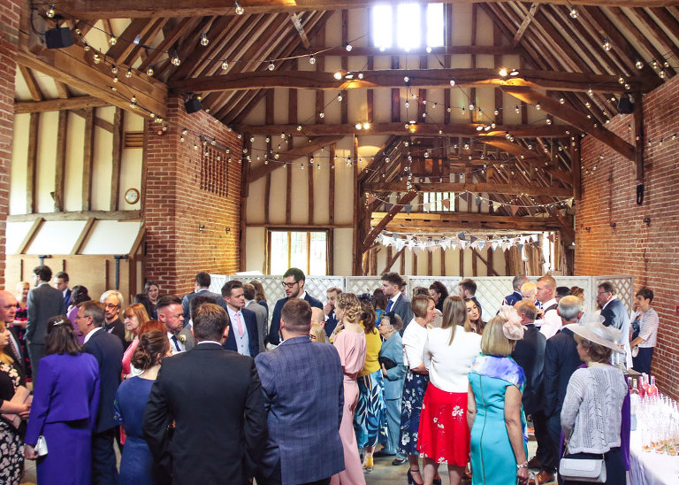 Wedding guests mingling in the barn during a wet wedding reception at Haughley Park Barn Wedding Venue photographed by Suffolk Wedding Photographers Hayley Denston Photography