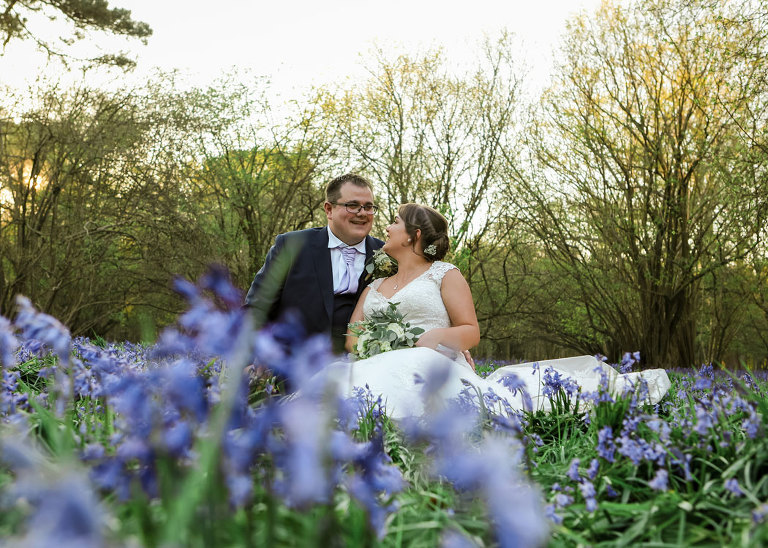 A bride and groom sat amongst the bluebells at Haughley Park Barn Wedding Venue photographed by Suffolk Wedding Photographers Hayley Denston Photography
