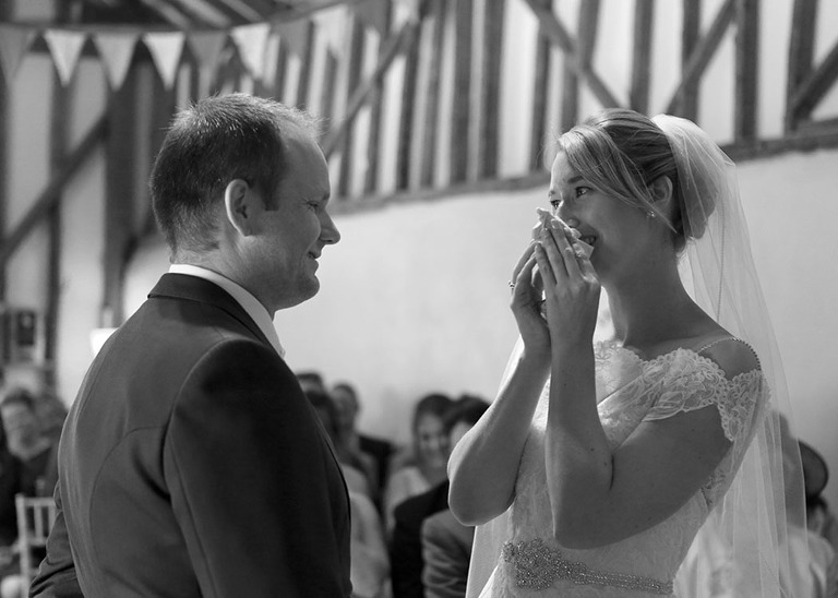 A bride and groom during their wedding ceremony with the bride wiping away her happy tears at Haughley Park Barn Wedding Venue photographed by Suffolk Wedding Photographers Hayley Denston Photography