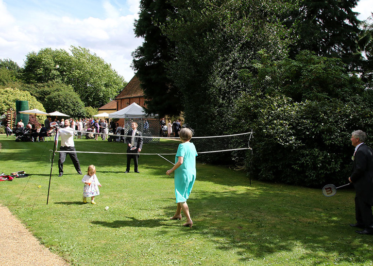 Guests playing badminton on the lawns on a summer wedding day at Haughley Park Barn Wedding Venue photographed by Suffolk Wedding Photographers Hayley Denston Photography