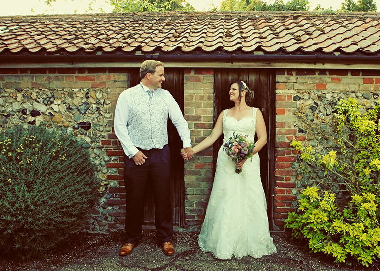 A bride and groom holding hands and looking at each other stood in front of a rustic shed at Haughley Park Barn Wedding Venue photographed by Suffolk Wedding Photographers Hayley Denston Photography