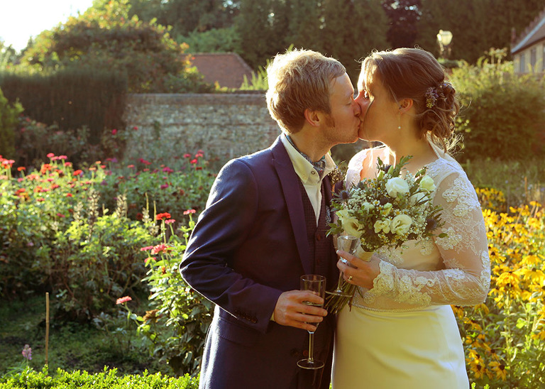 A bride and groom kissing in the autumnal kitchen garden in full flower at Haughley Park Barn Wedding Venue photographed by Suffolk Wedding Photographers Hayley Denston Photography