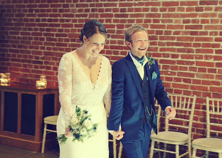 A bride and groom holding hands smiling and walking whilst they are introduced in to their wedding breakfast at Haughley Park Barn Wedding Venue photographed by Suffolk Wedding Photographers Hayley Denston Photography
