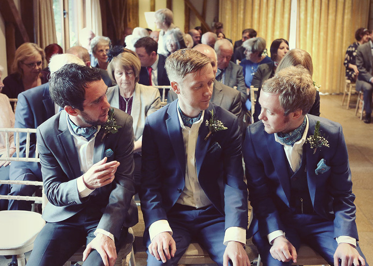 A groom and his bestmen waiting at the front of the ceremony room for his bride to arrive at Haughley Park Barn Wedding Venue photographed by Suffolk Wedding Photographers Hayley Denston Photography