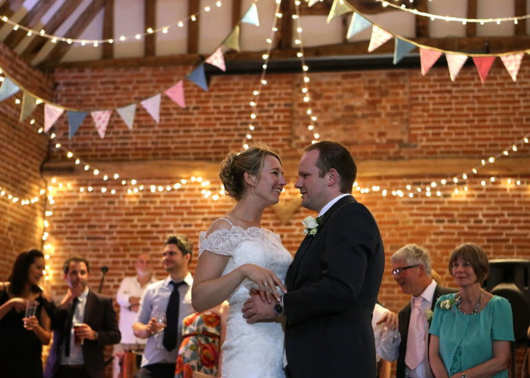A bride and groom having their first dance underneath pastel floral bunting at Haughley Park Barn Wedding Venue photographed by Suffolk Wedding Photographers Hayley Denston Photography