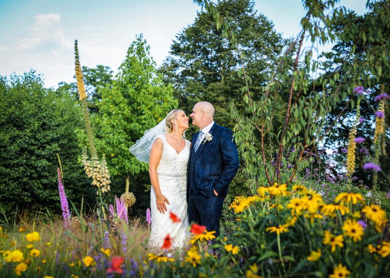 A bride and groom in a colourful flowerbed on the wedding day at the stunning Easton Grange Wedding Venue