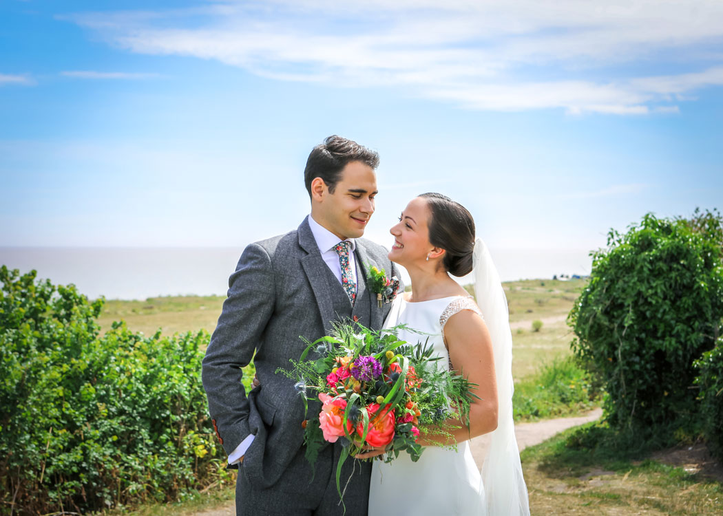 A bride and groom with the beach behind them on their wedding day in Suffolk photographed by Suffolk Wedding Photographers Hayley Denston Photography