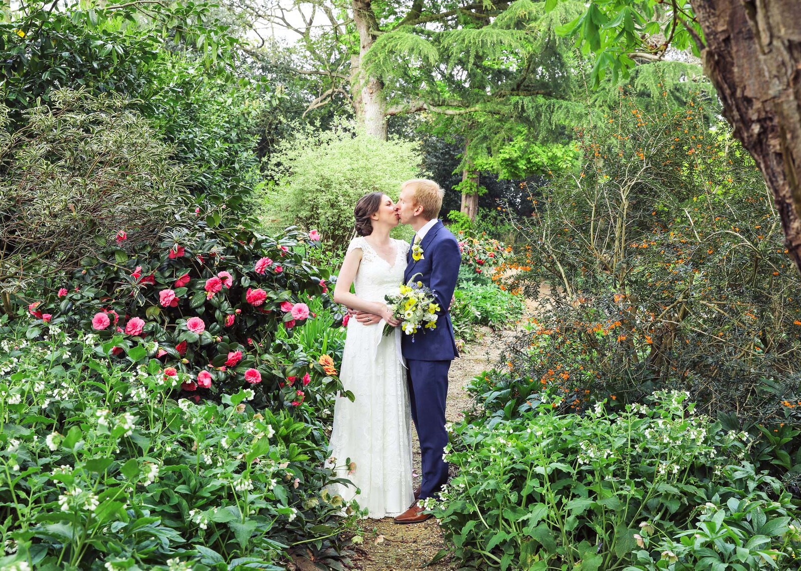 A bride and groom kissing in the woodland copse in spring on their wedding day at Haughley Park Barn Wedding Venue captured by Suffolk Wedding Photographers Hayley Denston Photography