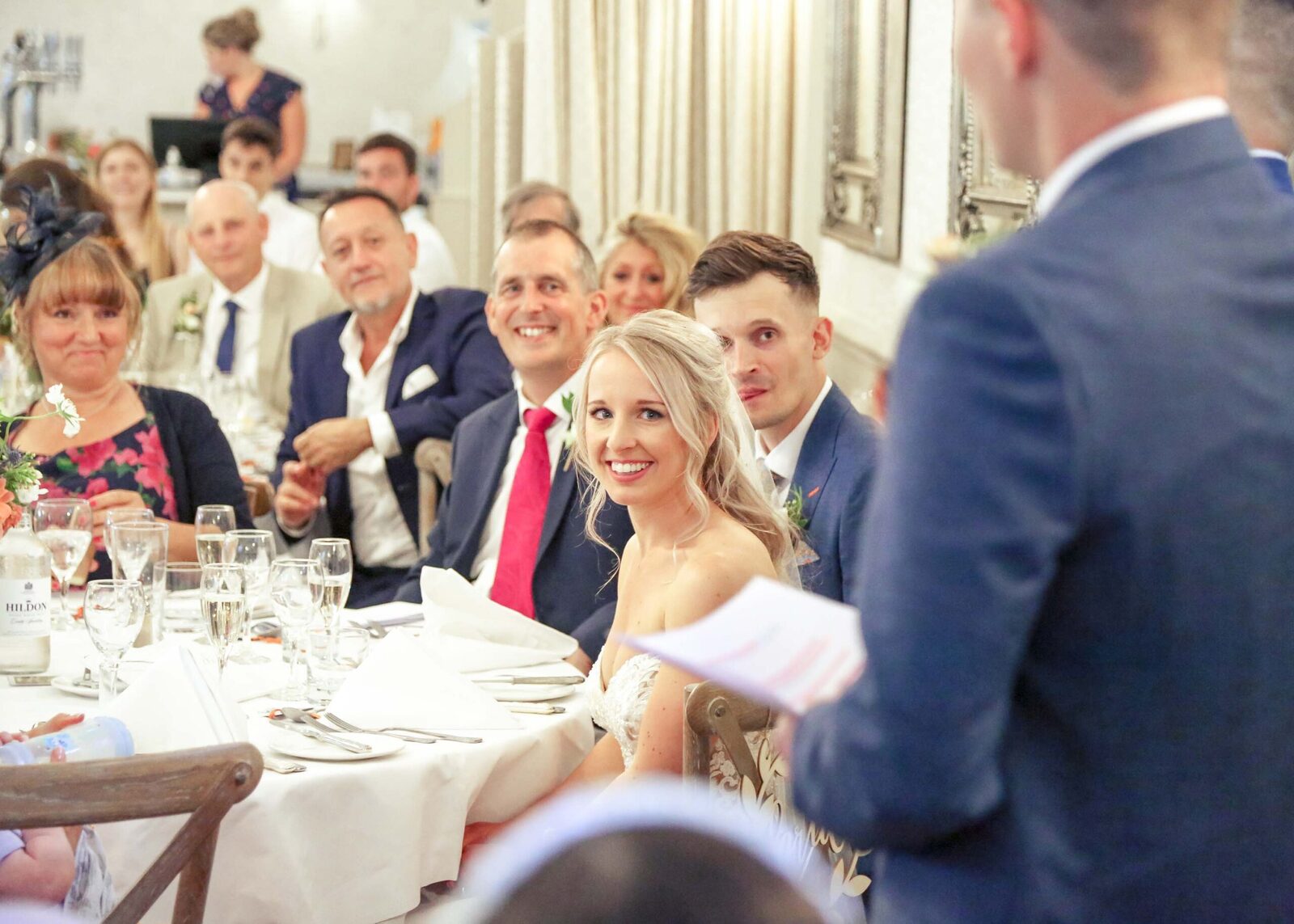 A bride and groom listening to the the bestmen giving speeches at their wedding at Ravenwood Hall Wedding Venue captured by Suffolk Wedding Photographers Hayley Denston Photography