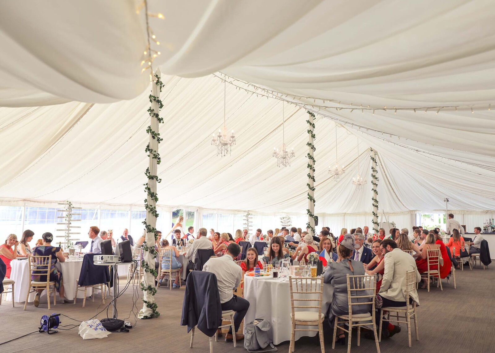 Inside a marquee set up for a wedding breakfast with guests sat at the tables captured by Suffolk Wedding Photographers Hayley Denston Photography