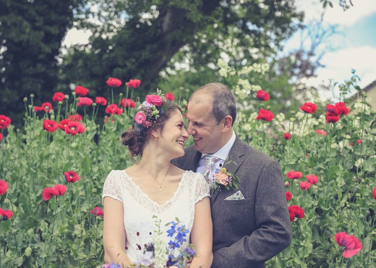 A bride and groom stood in front of a flower bed of bright pink poppies on their wedding day photographed by Suffolk Wedding Photographers Hayley Denston Photography