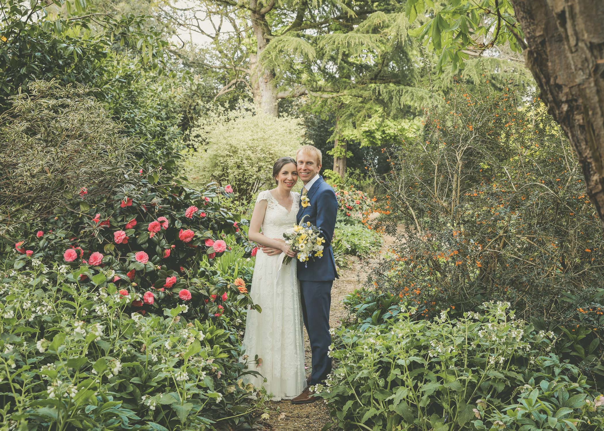 A bride and groom in the copse in spring flower on their wedding day at Haughley Park Barn Wedding Venue in Suffolk photographed by Suffolk Wedding Photographers Hayley Denston Photography