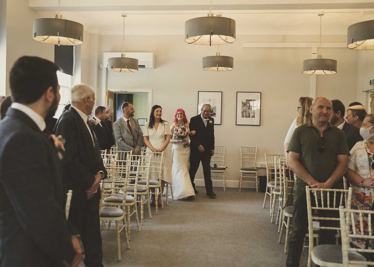 A bride and her dad walking down the aisle for her wedding ceremony at Bury St Edmunds Registry Office on a wedding day in Suffolk captured by Suffolk Wedding Photographers Hayley Denston Photography