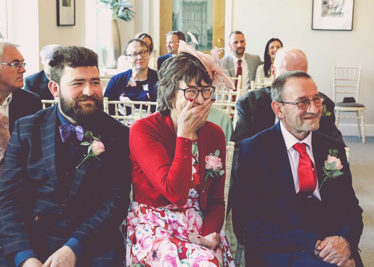 Guests laughing during a wedding ceremony at Bury St Edmunds Registry Office on a wedding day in Suffolk captured by Suffolk Wedding Photographers Hayley Denston Photography
