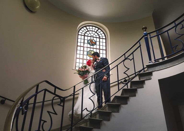 A bride and groom kissing on the stairs inside Bury St Edmunds Registry Office on their wedding day in Suffolk captured by Suffolk Wedding Photographers Hayley Denston Photography