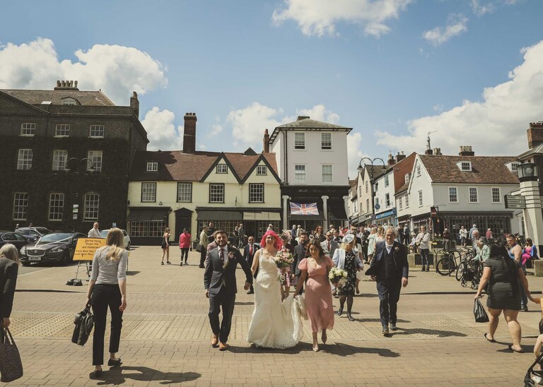 A bride and groom leading their wedding party through Bury St Edmunds to the Abbey Gardens on their wedding day in Suffolk captured by Suffolk Wedding Photographers Hayley Denston Photography