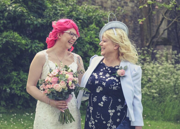 A bride and her mum looking and smiling at each other in the Abbey Gardens in Bury St Edmunds on a wedding day in Suffolk captured by Suffolk Wedding Photographers Hayley Denston Photography