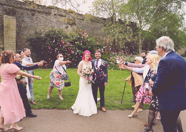 A bride and groom being showered in confetti by their guests in the Abbey Gardens in Bury St Edmunds on a wedding day in Suffolk captured by Suffolk Wedding Photographers Hayley Denston Photography