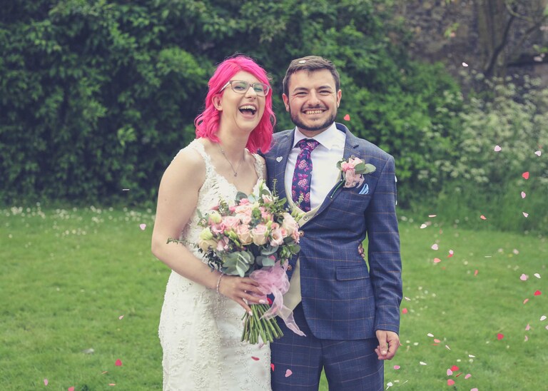 A bride and groom laughing during a confetti throw in the Abbey Gardens in Bury St Edmunds on a wedding day in Suffolk captured by Suffolk Wedding Photographers Hayley Denston Photography