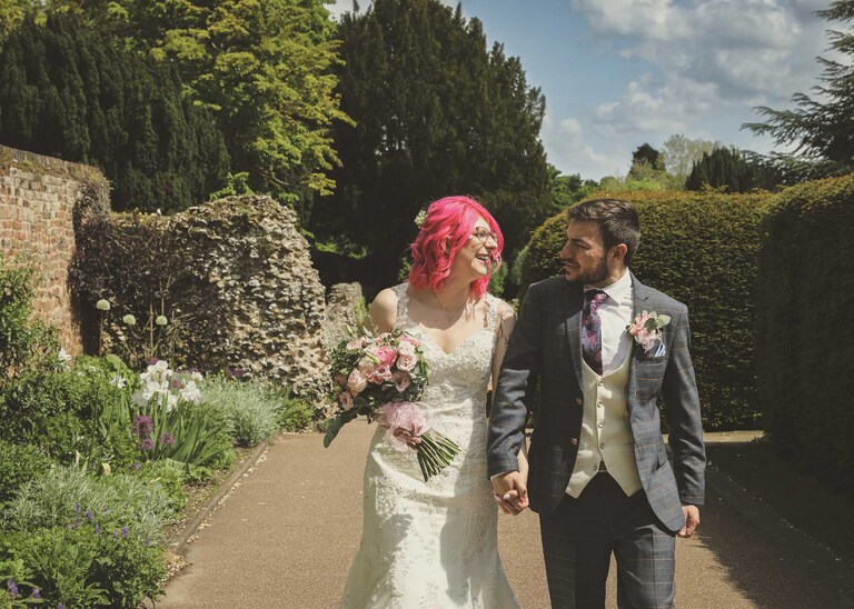 A bride and groom walking through the gardens hand in hand in the Abbey Gardens in Bury St Edmunds on a wedding day in Suffolk captured by Suffolk Wedding Photographers Hayley Denston Photography