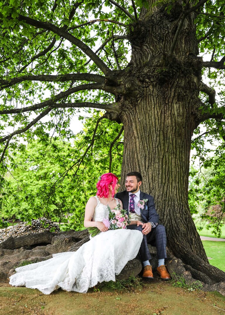 A bride and groom sat under an oak tree looking at each other in the Abbey Gardens in Bury St Edmunds on a wedding day in Suffolk captured by Suffolk Wedding Photographers Hayley Denston Photography