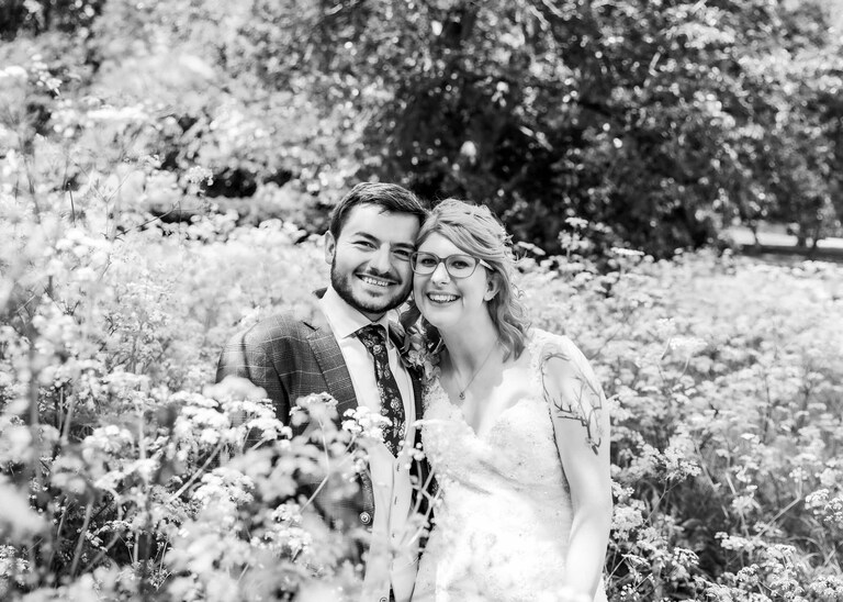 A bride and groom together in the Abbey Gardens in Bury St Edmunds in a flowerbed full of cow parsley on a wedding day in Suffolk captured by Suffolk Wedding Photographers Hayley Denston Photography