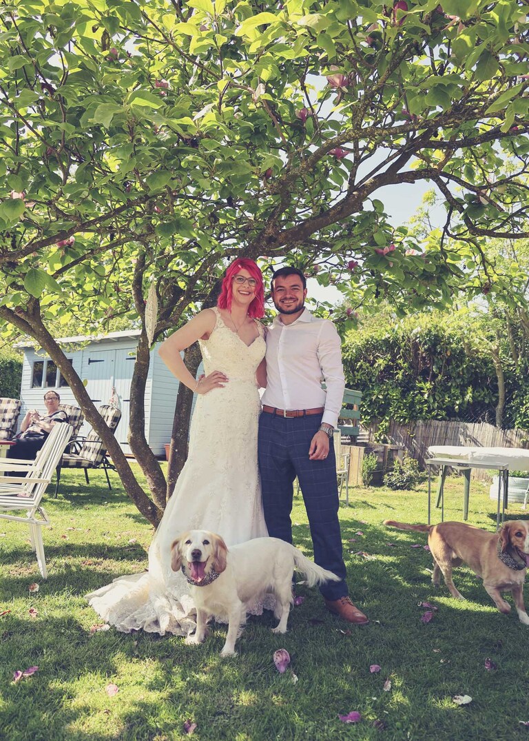 A bride and groom and their dogs under a magnolia tree during a wedding reception on a wedding day in Suffolk captured by Suffolk Wedding Photographers Hayley Denston Photography
