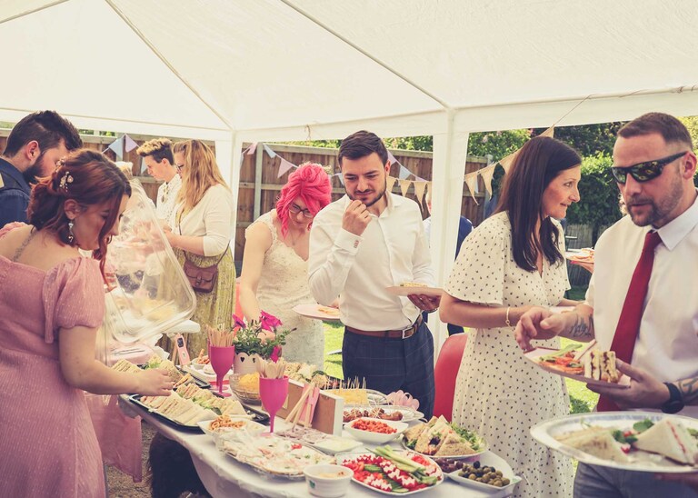 The bride and groom and wedding guests selecting food from a wedding reception buffet on a wedding day in Suffolk captured by Suffolk Wedding Photographers Hayley Denston Photography