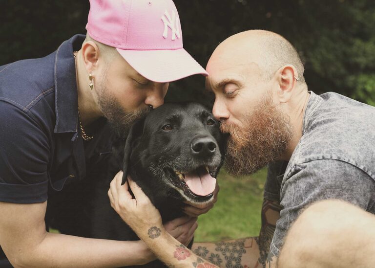 Two men kissing their elderly black labrador at a suffolk pet portrait session by suffolk pet photographer hayley denston photography