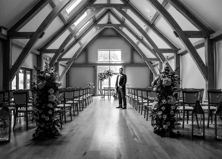 A groom waiting on his own in the ceremony barn before his wedding ceremony at Easton Grange on a Wedding Day photographed by Suffolk Wedding Photographers Hayley Denston Photography