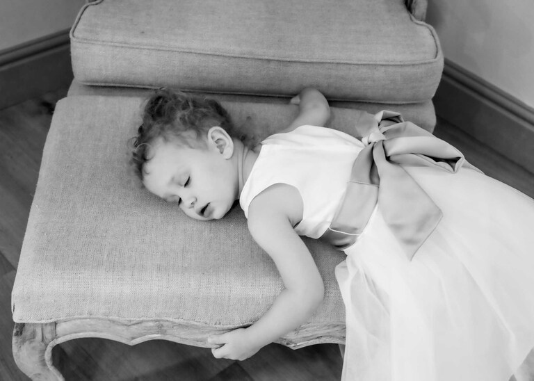A flowergirl having a nap on a chair during her parents wedding ceremony at Easton Grange on a Wedding Day photographed by Suffolk Wedding Photographers Hayley Denston Photography