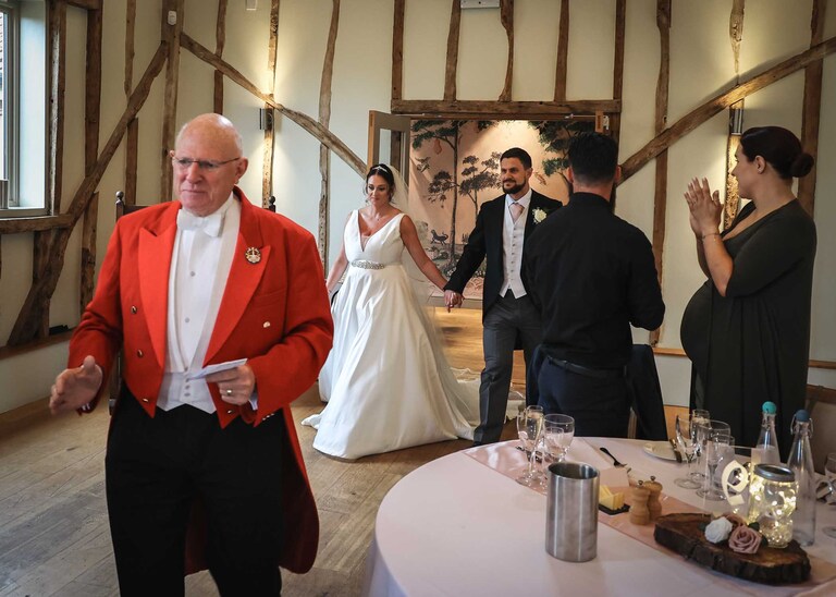 A toastmaster leading in the bride and groom to their wedding breakfast at Easton Grange on a Wedding Day photographed by Suffolk Wedding Photographers Hayley Denston Photography