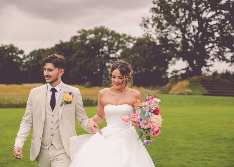 A bride and groom walking in the rain holding hands at Easton Grange Wedding Venue on a wedding day photographed by Suffolk Wedding Photographers Hayley Denston Photography