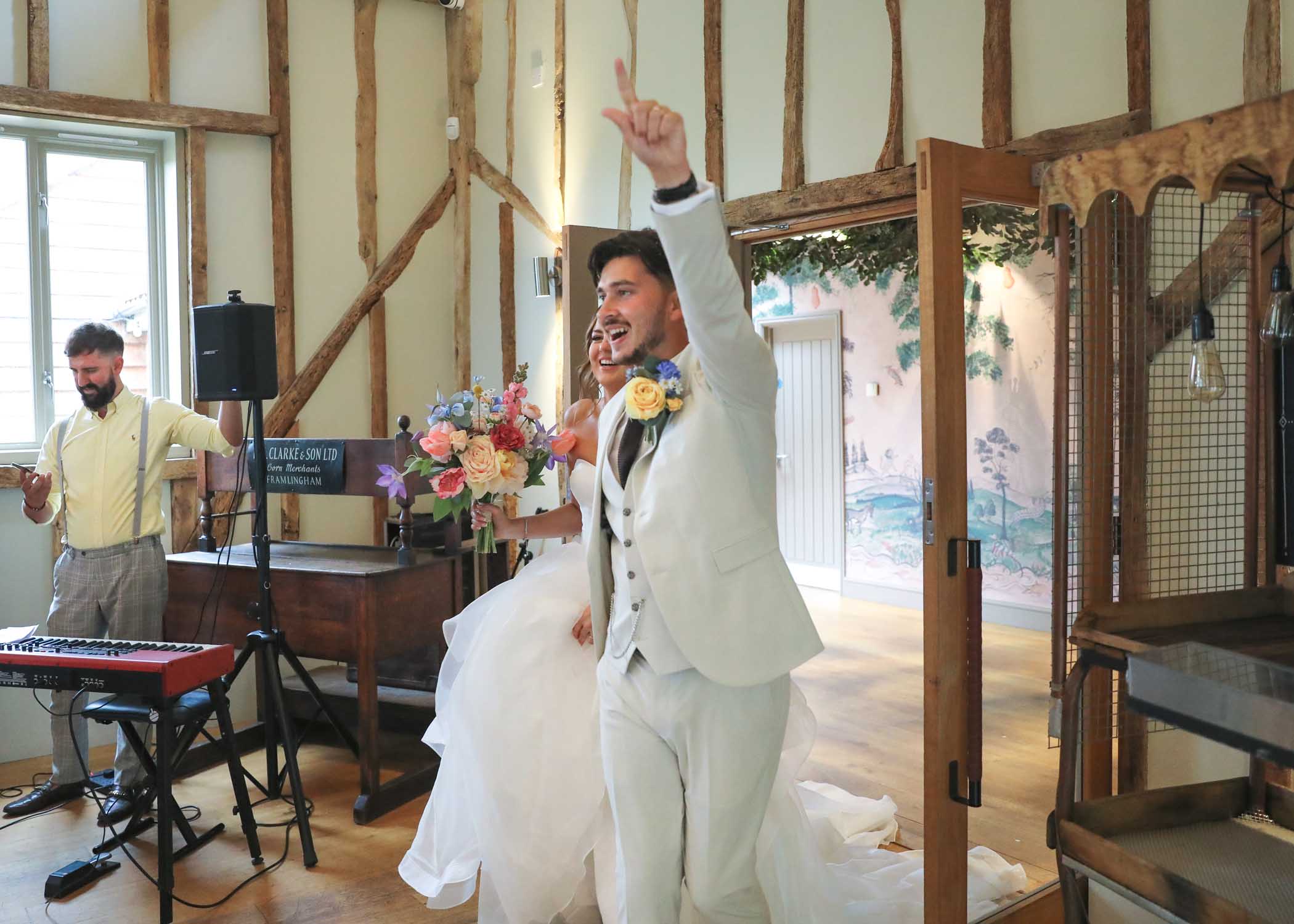 A bride and groom entering their wedding breakfast with the groom pointing at the ceiling at Easton Grange Wedding Venue on a wedding day photographed by Suffolk Wedding Photographers Hayley Denston Photography
