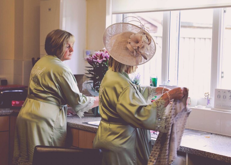 A mother of the bride and of the groom doing the washing up on a wedding day at Hungarian Hall on a Wedding Day photographed by Suffolk Wedding Photographers Hayley Denston Photography