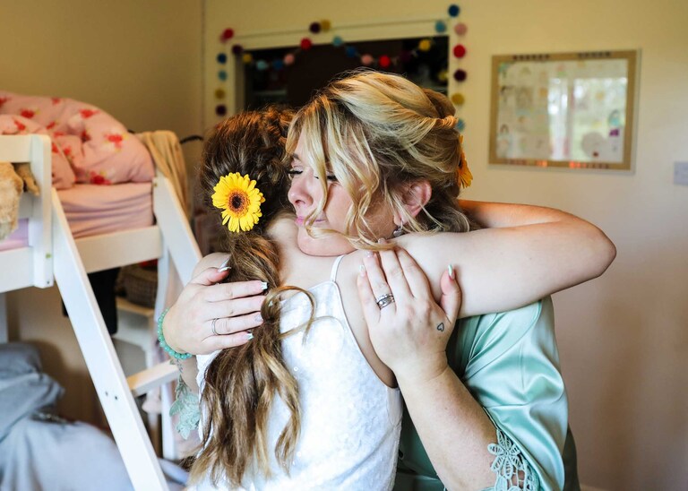 A bridesmaid cuddling the flowergirl at Hungarian Hall on a Wedding Day photographed by Suffolk Wedding Photographers Hayley Denston Photography