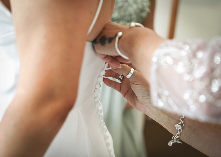 A close up of buttons on a wedding dress being done up at Hungarian Hall on a Wedding Day photographed by Suffolk Wedding Photographers Hayley Denston Photography