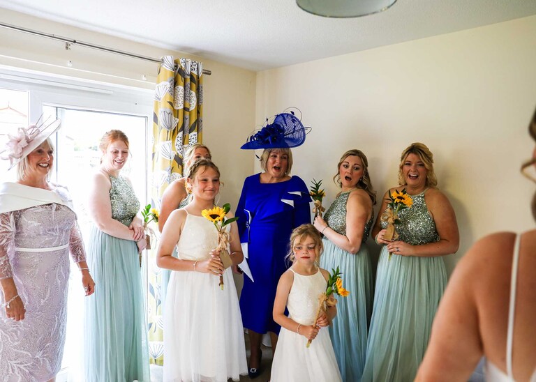The bridesmaids, mums and flowergirls seeing the bride in her wedding dress at Hungarian Hall on a Wedding Day photographed by Suffolk Wedding Photographers Hayley Denston Photography