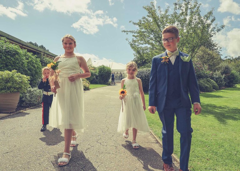 The flowergirls and pageboys walking down to meet the bride on her arrival for her wedding ceremony at Hungarian Hall on a Wedding Day photographed by Suffolk Wedding Photographers Hayley Denston Photography