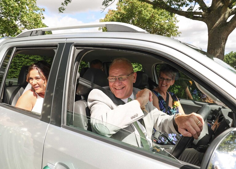 A bride arriving with her aunt, uncle and dad to her wedding ceremony ina smilver vehicle at Hungarian Hall on a Wedding Day photographed by Suffolk Wedding Photographers Hayley Denston Photography