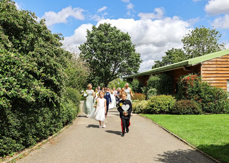A bridal party walking to the outdoor wedding ceremony at Hungarian Hall on a Wedding Day photographed by Suffolk Wedding Photographers Hayley Denston Photography