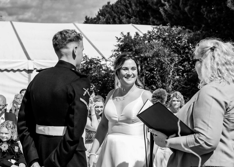 A bride smiling at the registrar during her outdoor wedding ceremony at Hungarian Hall on a Wedding Day photographed by Suffolk Wedding Photographers Hayley Denston Photography