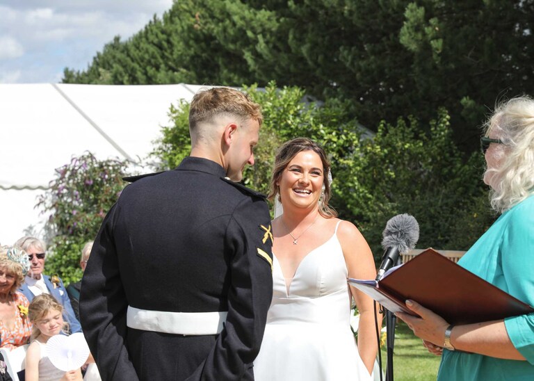 A bride and groom laughing looking at the registrar during their outdoor wedding ceremony at Hungarian Hall on a Wedding Day photographed by Suffolk Wedding Photographers Hayley Denston Photography