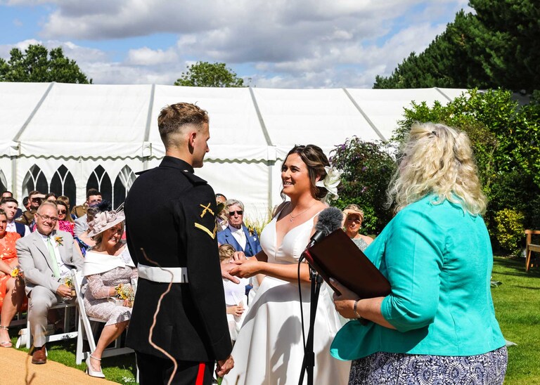 A bride and groom exchanging wedding rings at an outdoor ceremony at Hungarian Hall on a Wedding Day photographed by Suffolk Wedding Photographers Hayley Denston Photography