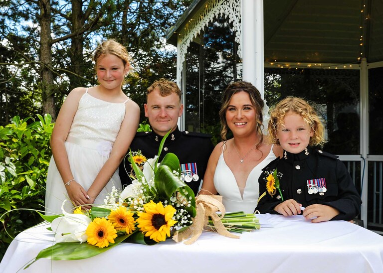 A bride and groom sat with their children after signing the register at Hungarian Hall on a Wedding Day photographed by Suffolk Wedding Photographers Hayley Denston Photography