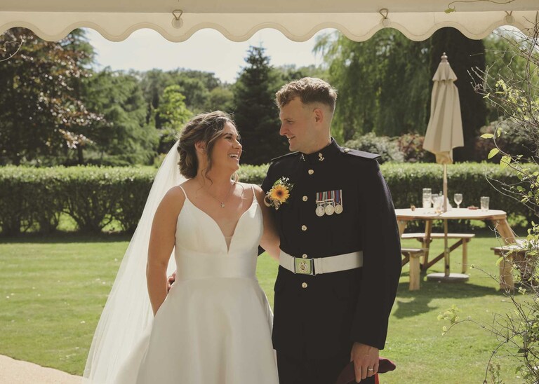 A bride and groom looking at each other laughing with their arms wrapped around each other before being announced in for their wedding breakfast at Hungarian Hall on a Wedding Day photographed by Suffolk Wedding Photographers Hayley Denston Photography